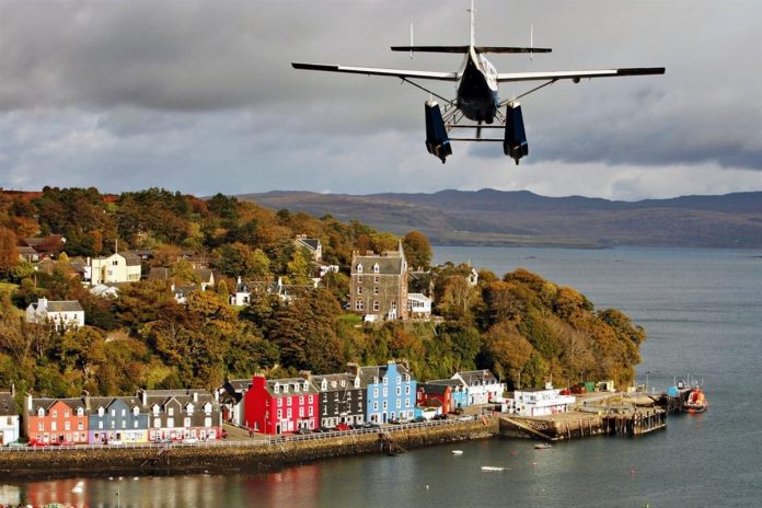 Un hydravion glisse au-dessus des maisons multicolores le long de la jetée de Tobermory, avec les collines de North Mull au-dessus de l'eau au loin. © VisitScotland - Paul Tomkins, all rights reserved
