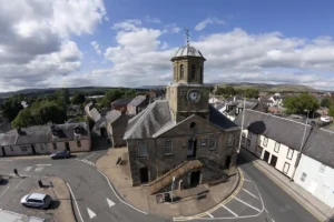 Sanquhar's picturesque Tollbooth museum, with dome and clock, seen diagonally from above, with rows of whitewashed cottages lining the square.