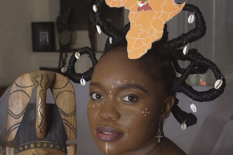 Femme portant une coiffe surmontée d’une carte de l’Afrique, tenant un masque en bois sculpté